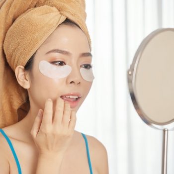 Asian woman with under-eye patches applying makeup