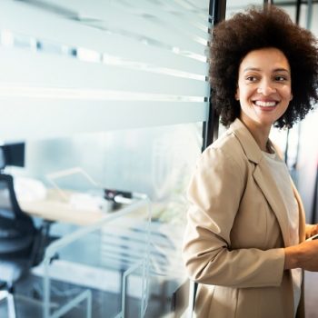 Portrait of an attractive young african businesswoman smiling while standing by windows in office