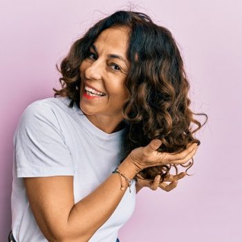 Beautiful hispanic woman curling hair using cosmetics products, doing curly style treatment on hair
