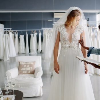 Dress designer fitting bridal gown to woman in boutique