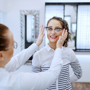Female optician putting eyeglasses on beautiful Caucasian smilin