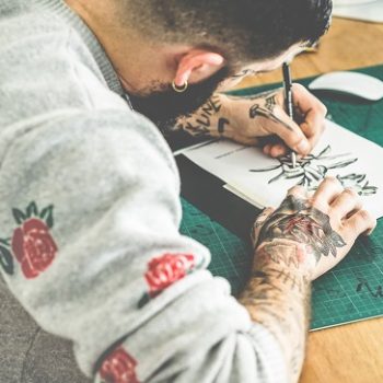 Young tattoo artist drawing sketch inside ink studio – Hipster t